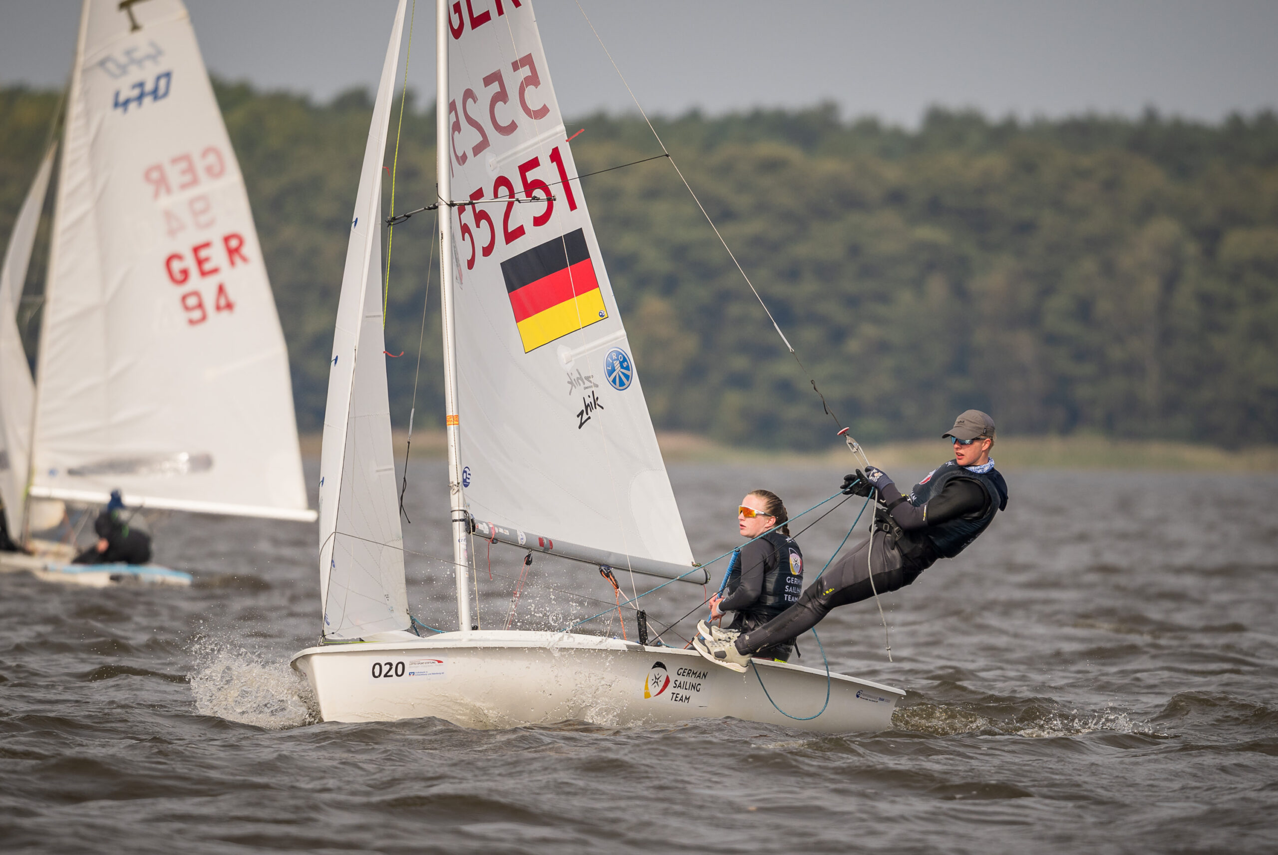 Eine Seglerin und ein Segler auf einer 420er Jolle, Auf dem Rumpf steht German Sailing Team, im Segel ist die Nummer 55251, eine Deutschlandflagge und die Logos von zwei Sponsoren.