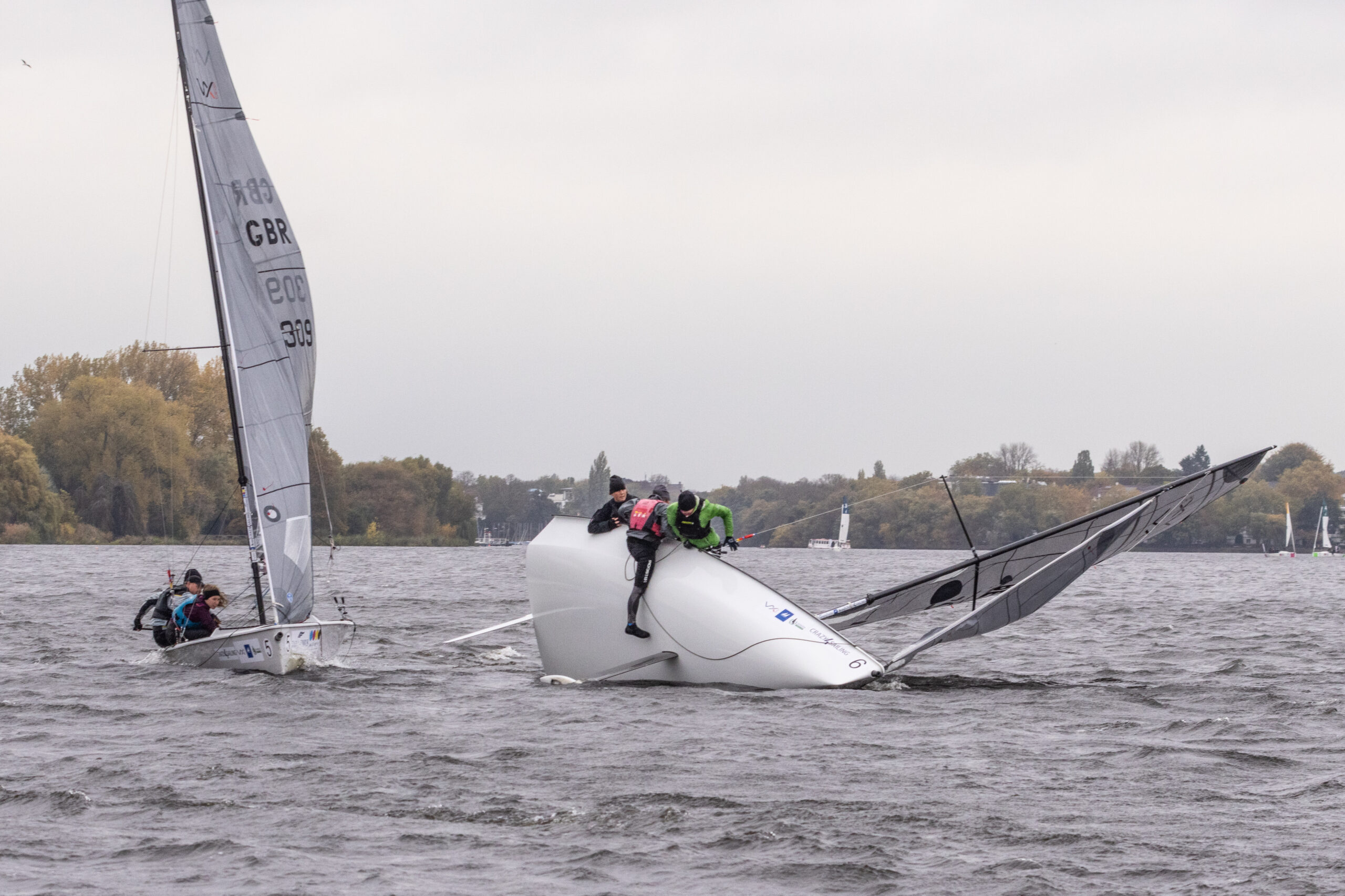 Eine Kielschwertyacht kentert auf der Hamburger Außenalster, die Crew versucht über den Rumpf auf das Schwert zu klettern.