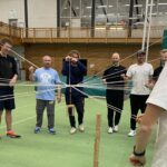 Mehrere Männer ziehen in einer Sporthalle an Fäden.