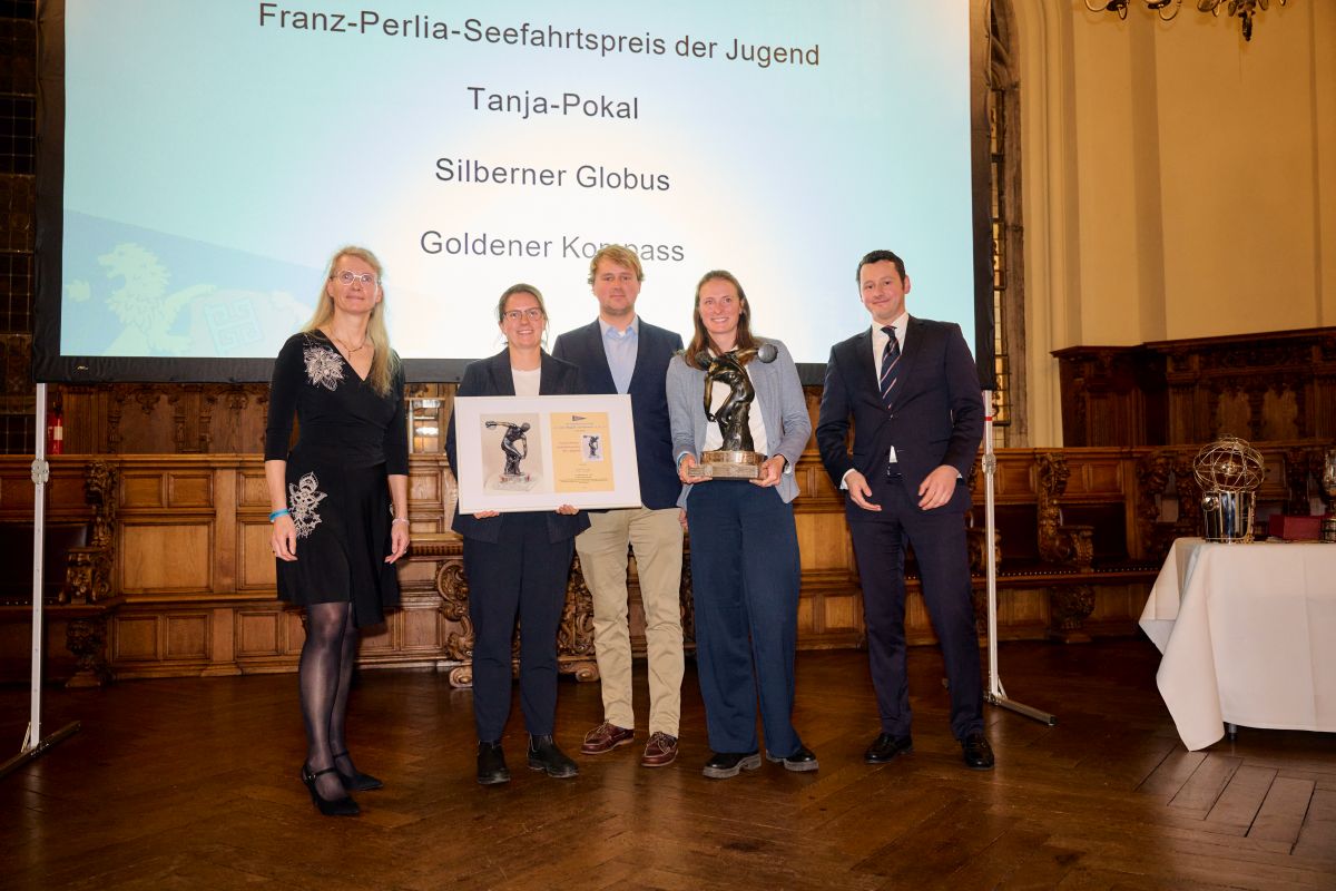 Fünf junge Menschen stehen bei einer Preisverleihung. Eine Frau hält einen Preis in den Händen, der eine Figur mit einem Diskus zeigt.