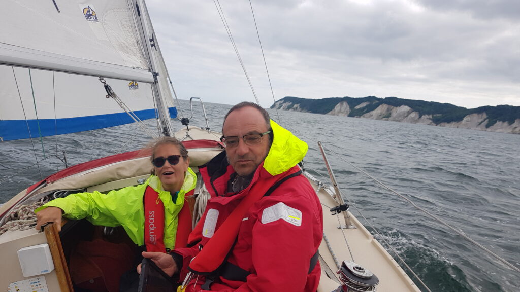 Eine Seglerin in ein Segler sitzen mit Rettungsweste und Ölzeug auf dem Folkeboot.