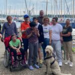 Eine Gruppe von Menschen mit und ohne Behinderung stehen zusammen und freuen sich über ihren gemeinsamen Tag auf dem Wasser