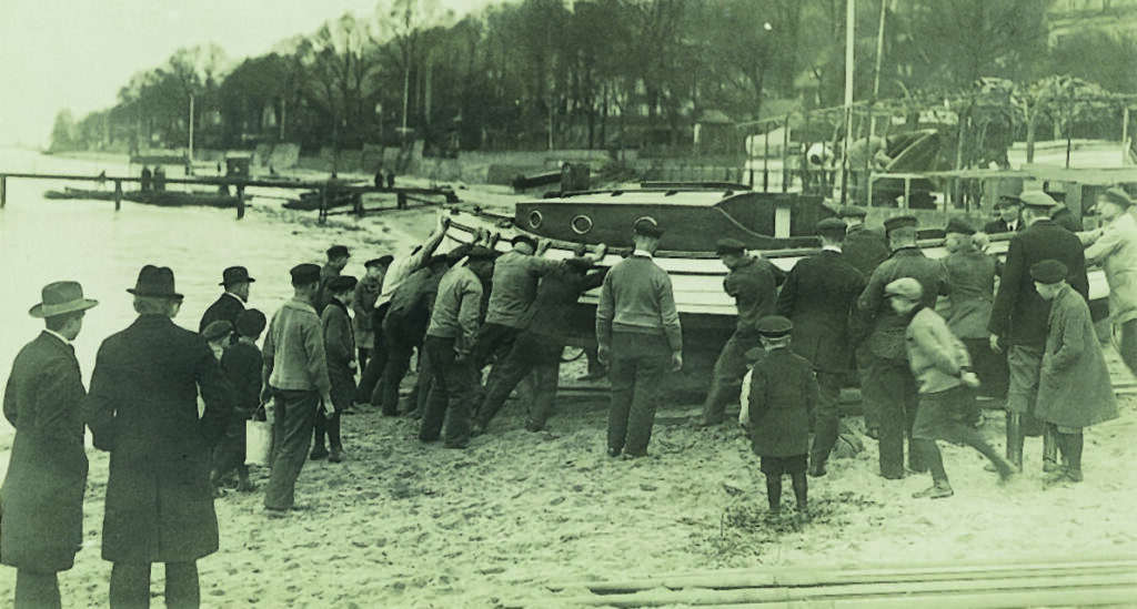 Historisches Bild: Viele Menschen schieben per Hand ein Holzboot den Elbstrand hinauf.