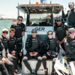 Das deutsche SailGP Team auf einem Motorboot, sie tragen schwarze Bekleidung und das Logo der Deutschen Bank
