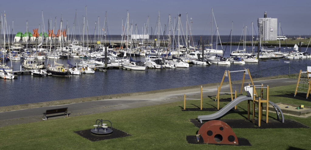 Im Hintergrund liegen Segelboote an Stegen, im Vordergrund ist ein Spielplatz für Kinder.