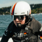 Eine Seglerin mit weißem Helm und schwarzer Bekleidung, auf ihrem Oberteil ist die deutsche Flagge und GER zu erkennen.