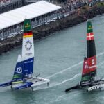 Drei foilende F50-Katamarane mit bunten Segeln vor einer voll besetzten Zuschauertribüne