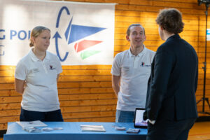 Eine Person informiert sich bei einem Stand der Turning Point Stiftung zum Thema inklusives Segeln. Zwei Engagierte der Stiftung geben dabei Auskunft.