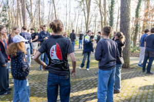 Junge Menschen stehen draußen in einem Kreis während eines Workshops. Eine Teilnehmerin wirft dabei einen Ball zu einer anderen Person.