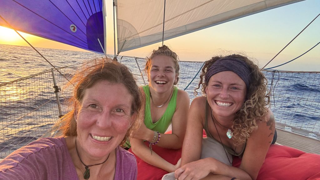 Drei Frauen liegen auf dem Deck einer segelyacht und lachen in die Kamera. Im Hintergrund sind Segel und die Sonne.