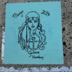 Auf einem blauen Papier ist eine Zigeunerin mit schwarzer Farbe gezeichnet, sie trägt ein Kopftuch und große Ohrringe. Die Zeichnung ist das Logo der Segelyacht mit dem Namen GITANA, die Zigeunerin