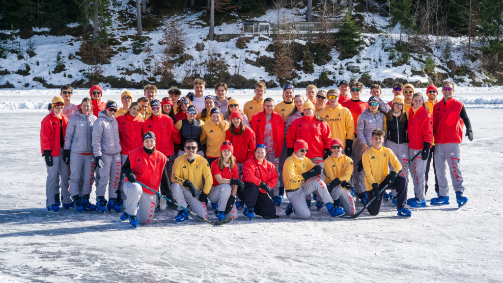 Teilnehmende des Deutschen Olympischen Jugendlagers in Milano Cortina stehen auf einem zugefrorenen See für ein Gruppenfoto. Sie tragen Schlittschuhe und schauen in die Kamera.