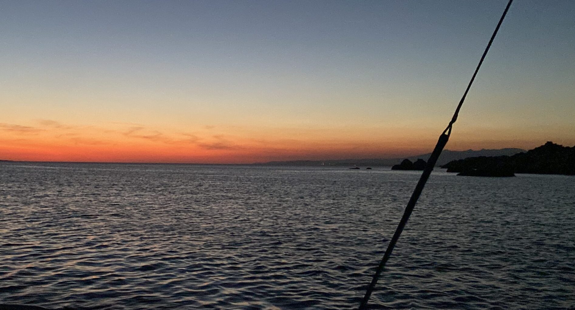 Ein stimmungsvoller Sonnenuntergang auf See, man kann den Heckkorb und das Backstag der Yacht erkennen