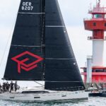 Eine Regattayacht vor einem rot-weißen Leuchtturm