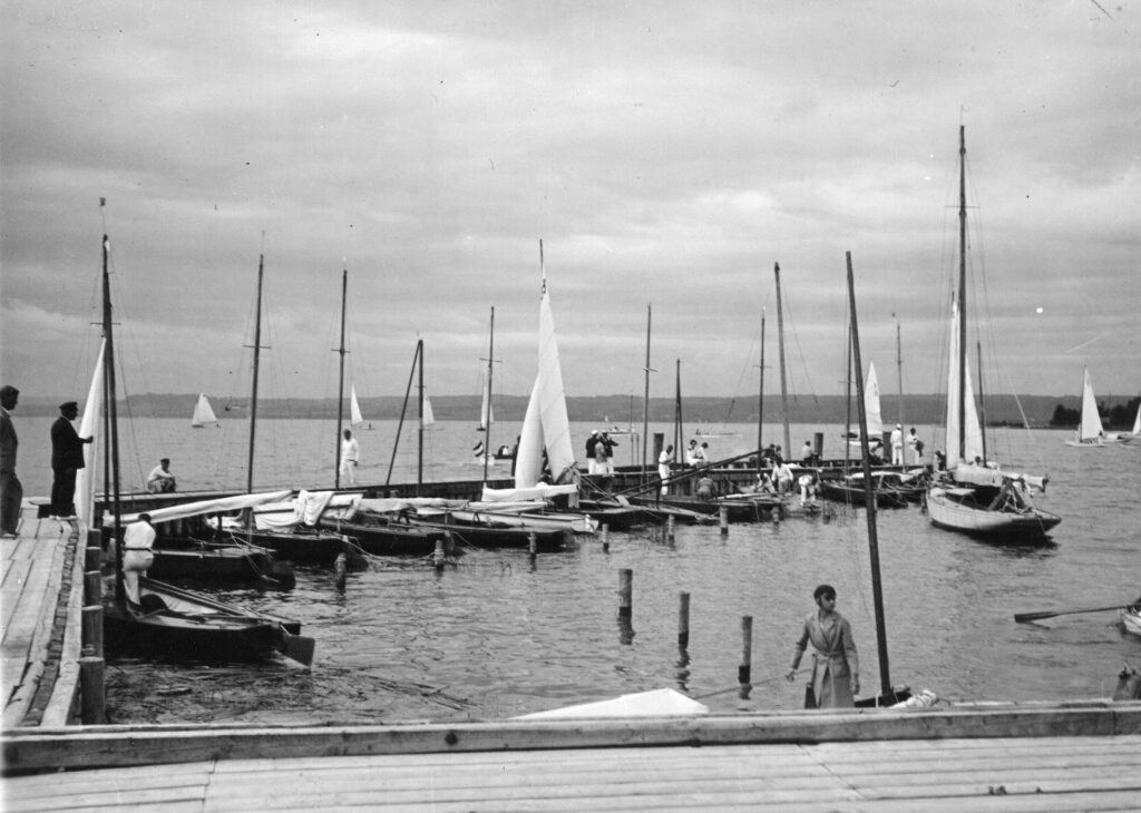 Dieses ist ein historisches schwarz-weiß Foto, es stammt aus den 1930er Jahren. An einem Holzsteg an einem See liegen kleine Jollen.