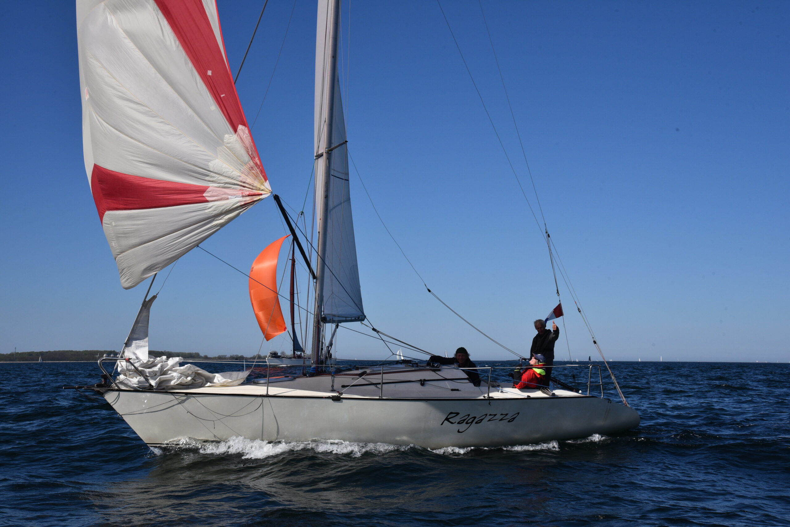 Eine Regattayacht vom Typ Banner 28 mit einem weißen Rumpf und einem rot-weißen Spinnaker.
