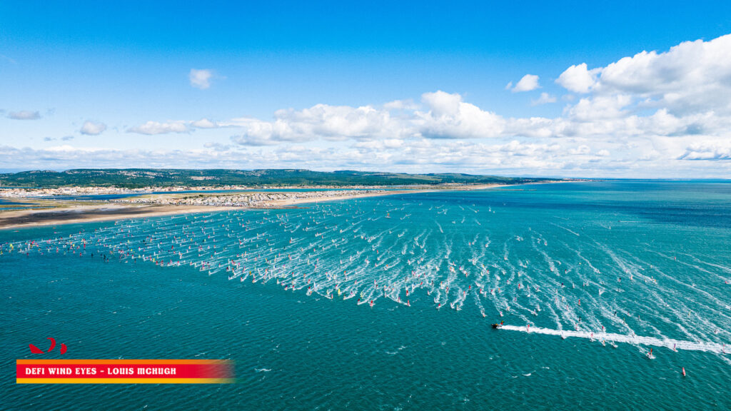 Viele Windsurfende sind zur gleichen Zeit auf dem Wasser. Sie starten alle zur gleichen Zeit in ein Rennen.