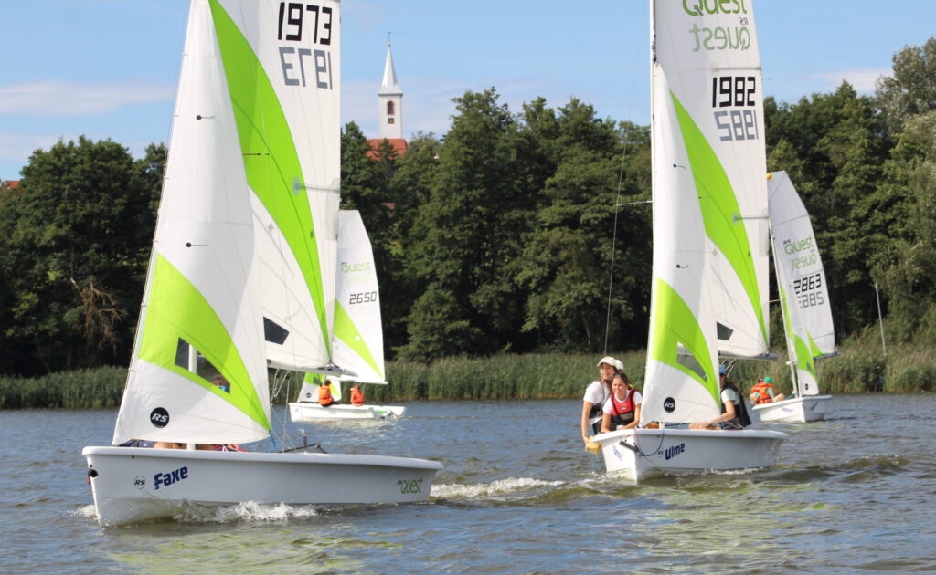 Junge Menschen segeln auf einem Teich. Die Segel sind weiß und grün.