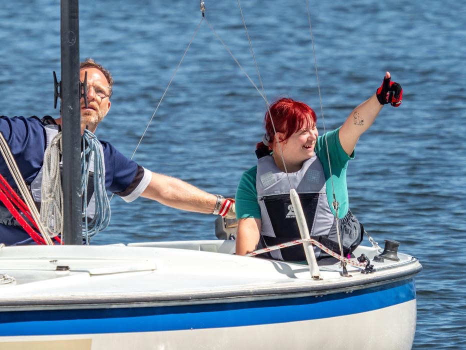 Ein Mann und eine Frau sitzen im Cockpit eines Segelboots. Die Seglerin freut sich und reckt den Daumen in die Höhe.