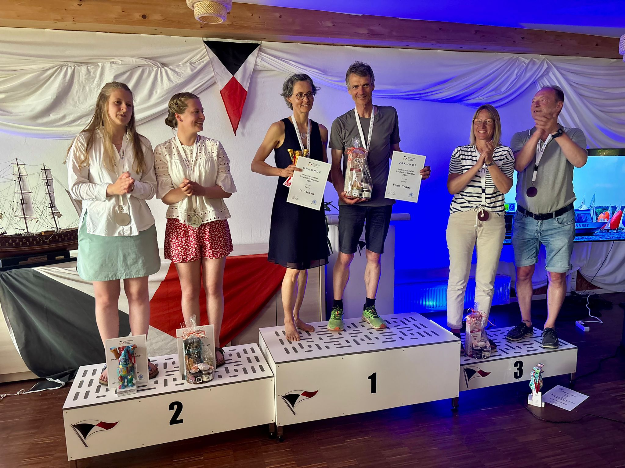 Drei erfolgreiche Teams stehen nach einer Regatta auf dem Podest, in der Mitte die Meister der Korsar-Klasse Uti und Frank Thieme