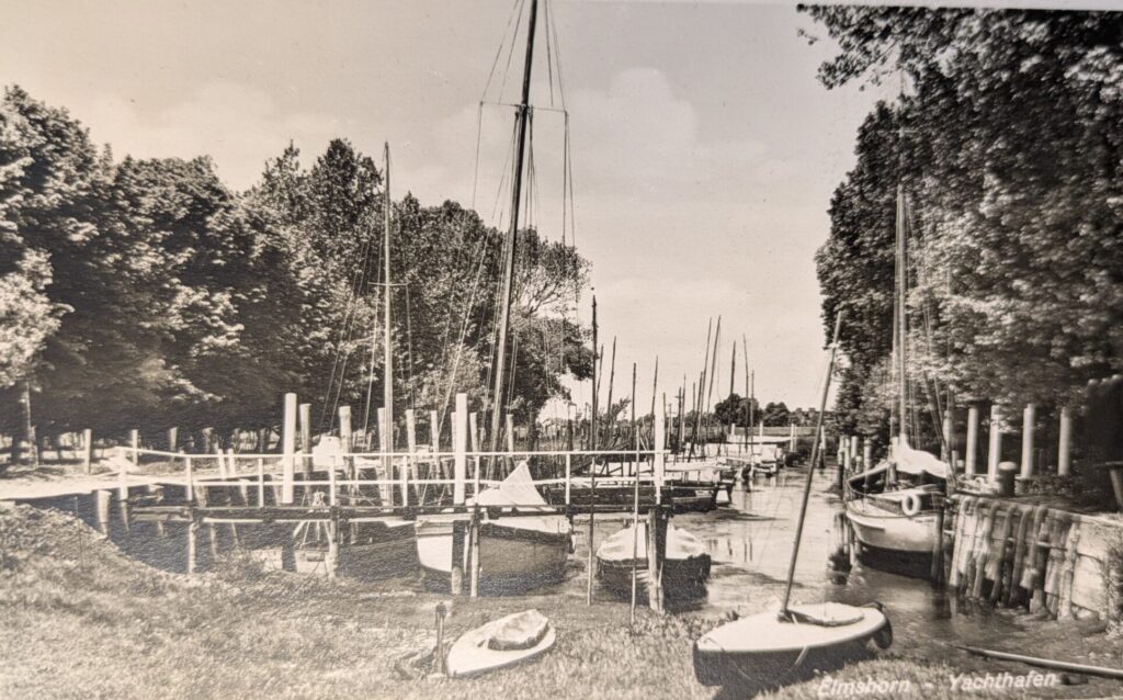 Das historische Schwarz-Weiß-Foto zeigt Segelboote in einem Hafen. Einige liegen am Steg, einige auf dem Rasen an Land.