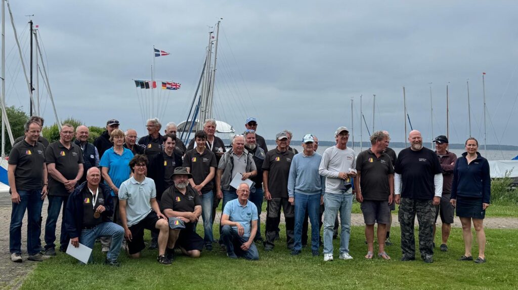 Eine Gruppe von Frauen und Männern stehen auf dem Rasen an einem Yachthafen