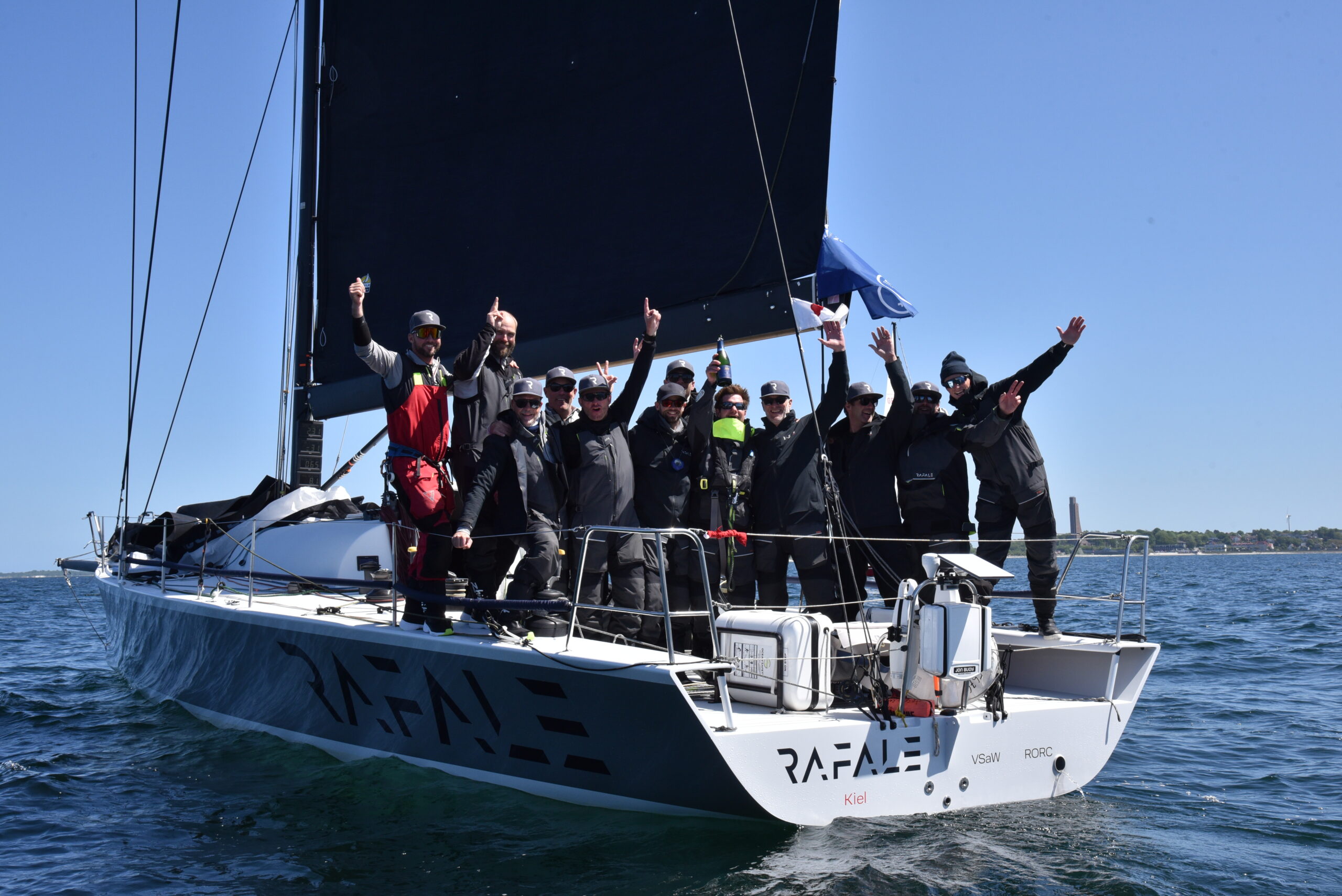 Die Crew einer Yacht jubelt im Heck stehend über einen Erfolg bei einer Regatta.
