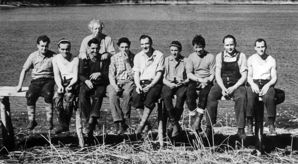 Das historische Schwarz-Weiß-Foto zeigt zehn Männer, die auf einem Balken sitzen.