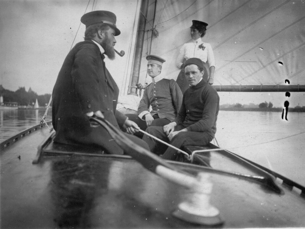 Das historische schwarz-weiß Foto zeigt Männer im Cockpit eines Segelbootes.