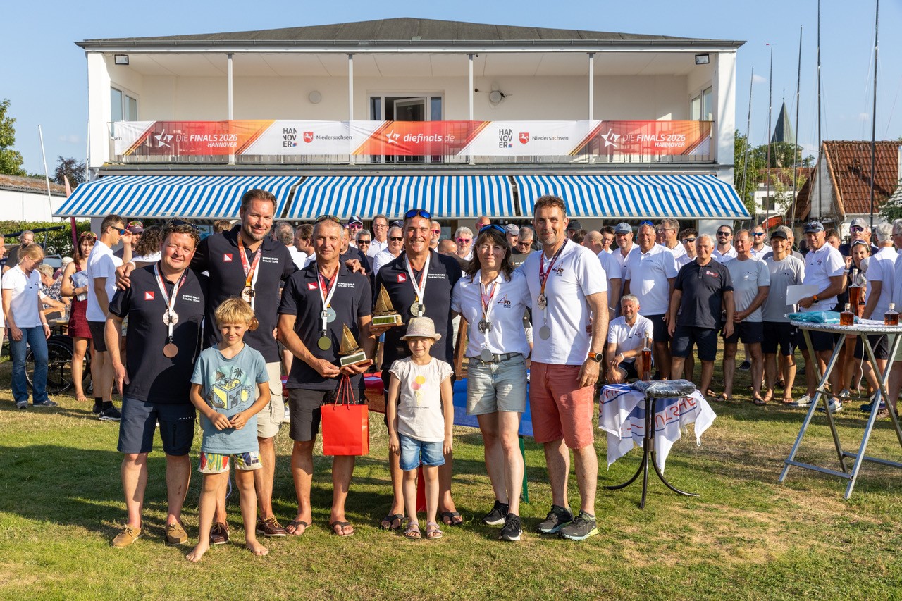 Sechs Menschen die bei einer Regatta gewonnen haben vor dem Clubhaus des HYC mit Medaillen um den Hals.