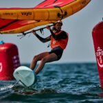 Eine Wingfoilerin surft über das Wasser, sie hält einen rot-orangen Wing.