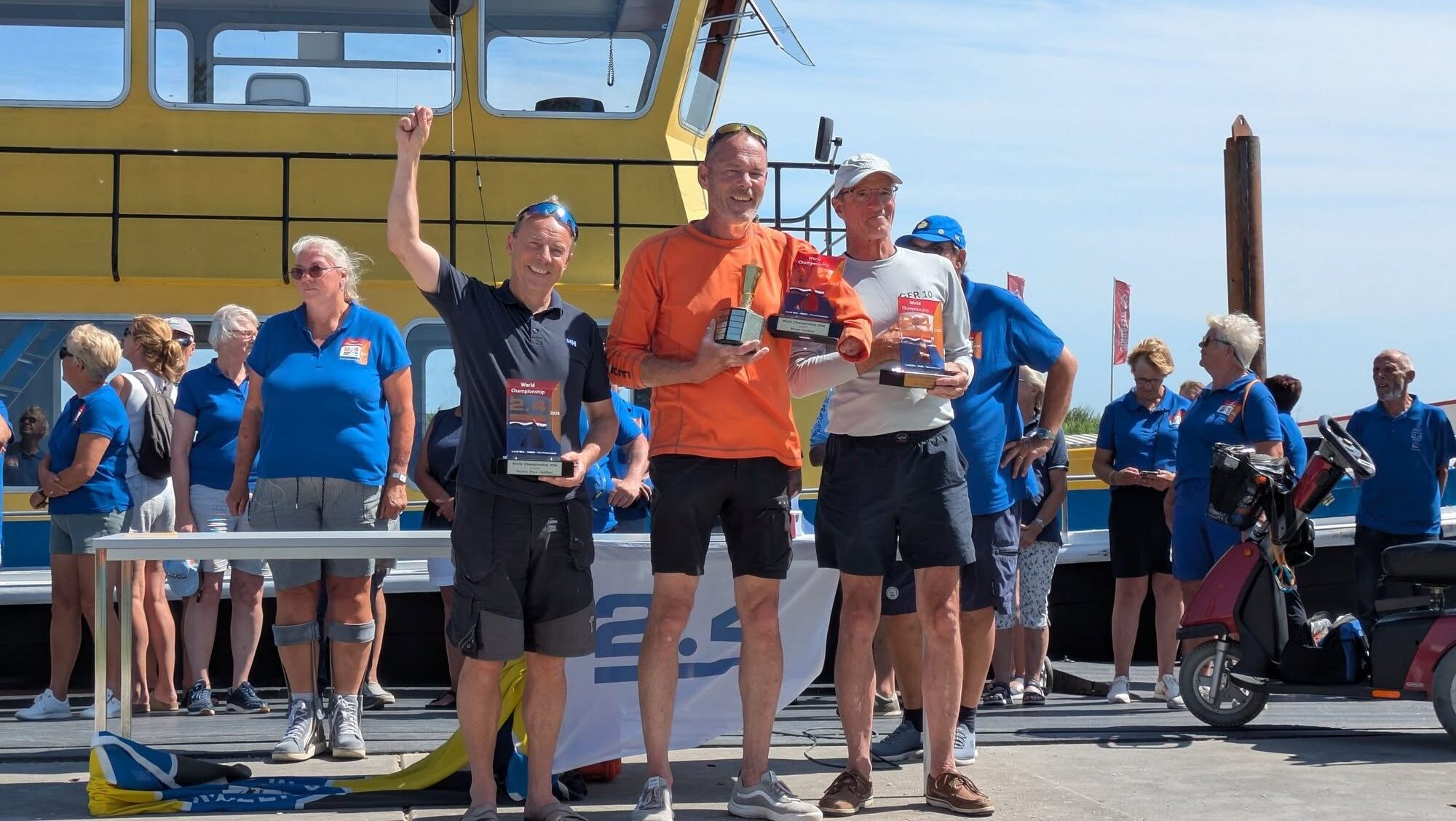 Drei Männer mit Trophäen nach einer Regatta in den Händen.