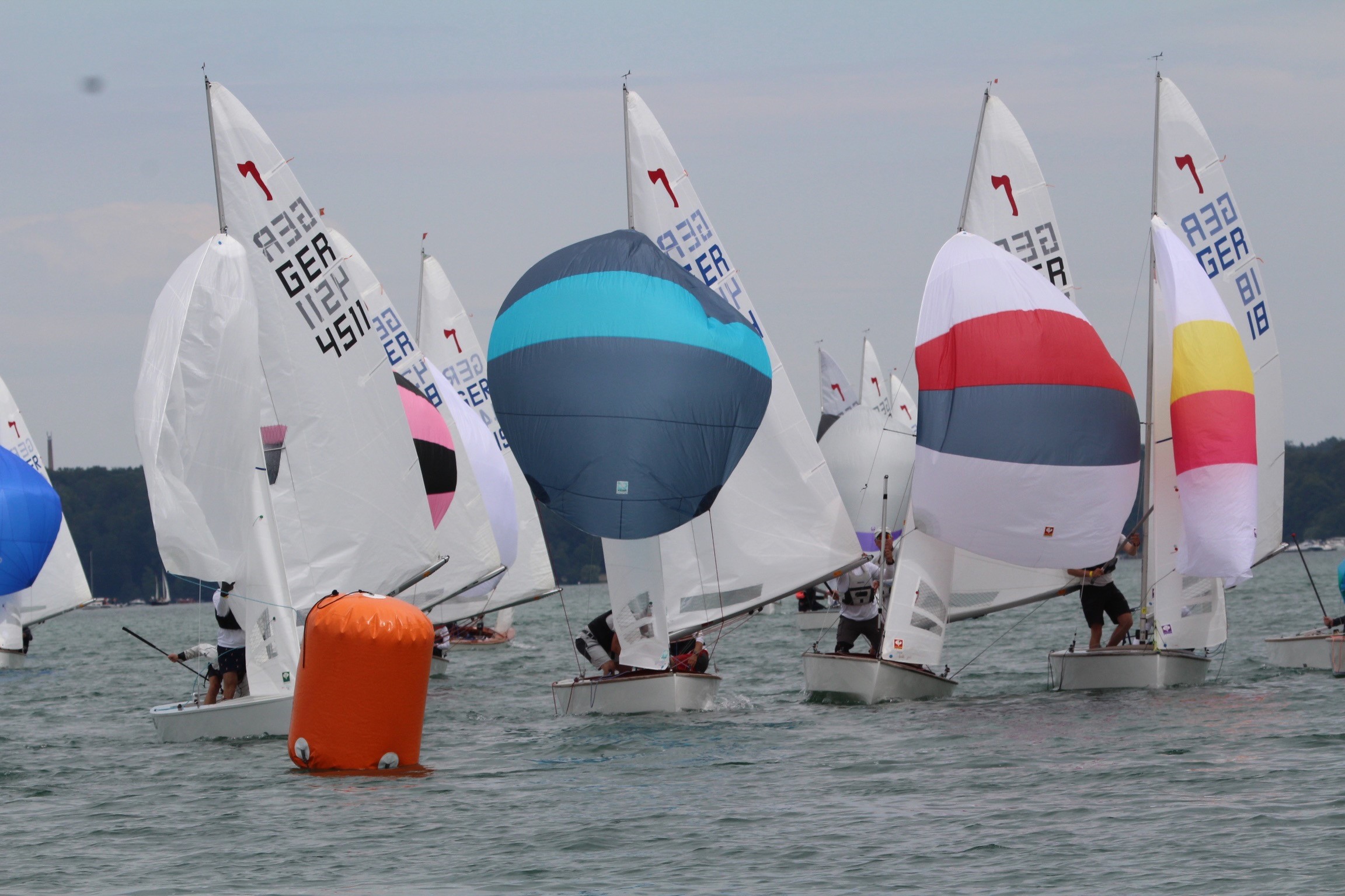 Viele Piratenjollen unter Spinnaker vor einer Wendemarke auf dem Wasser.