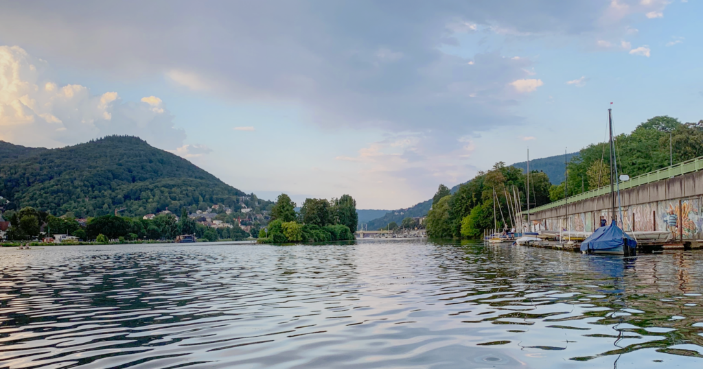Rechts am Ufer eines Flusses ist eine Steganlage, an der einige Boote liegen