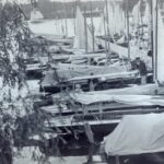 Das Foto ist ein historisches schwarz-weiß Bild. Frauen und Männer arbeiten an ihren Booten, die an einem Steg liegen.