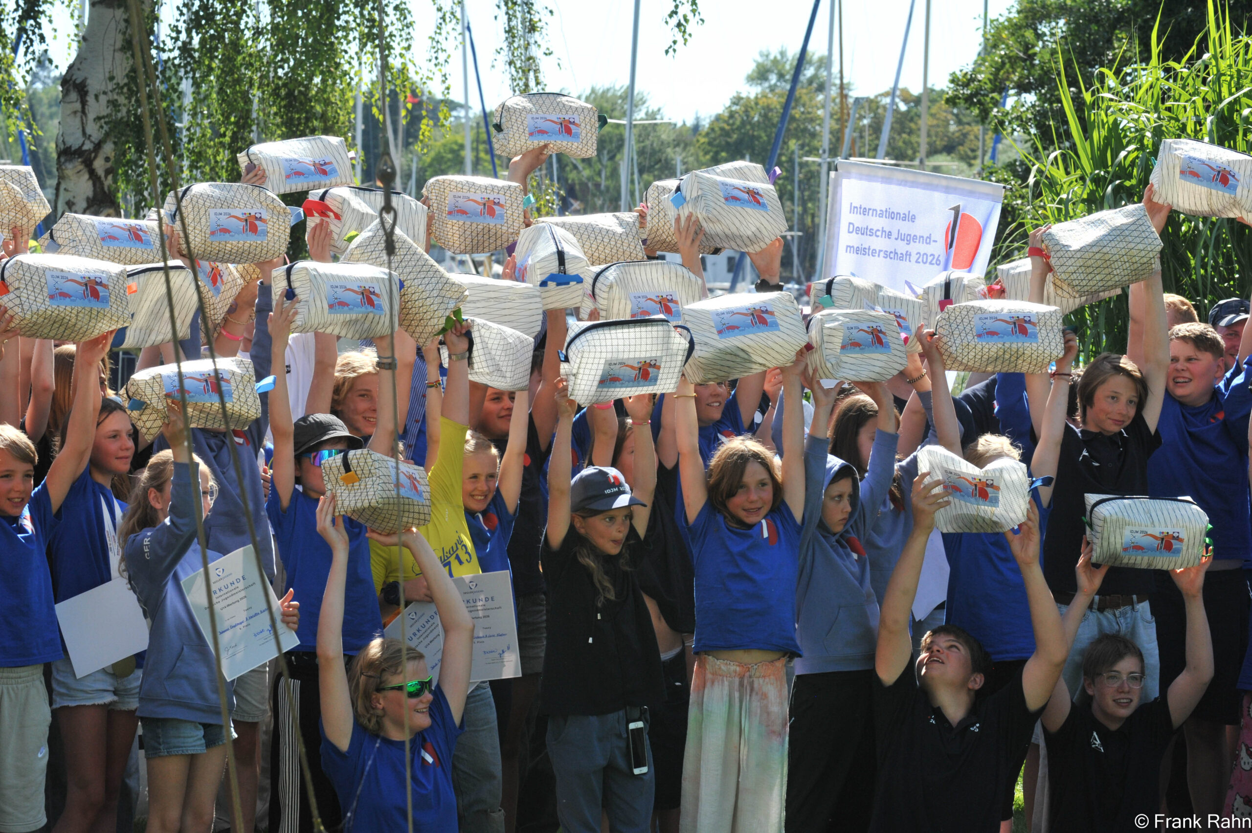 Viele Mädchen und Jungen strecken Kulturbeutel aus recyceltem Segeltuch in die Höhe.
