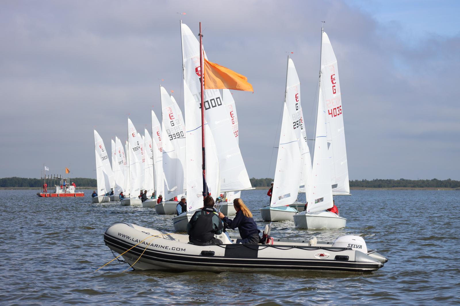 Mehrere Jollen vom Typ Conger stehen an der Startlinie vor dem Start zu einer Regatta, im Vordergrund ein graues Schlauchboot