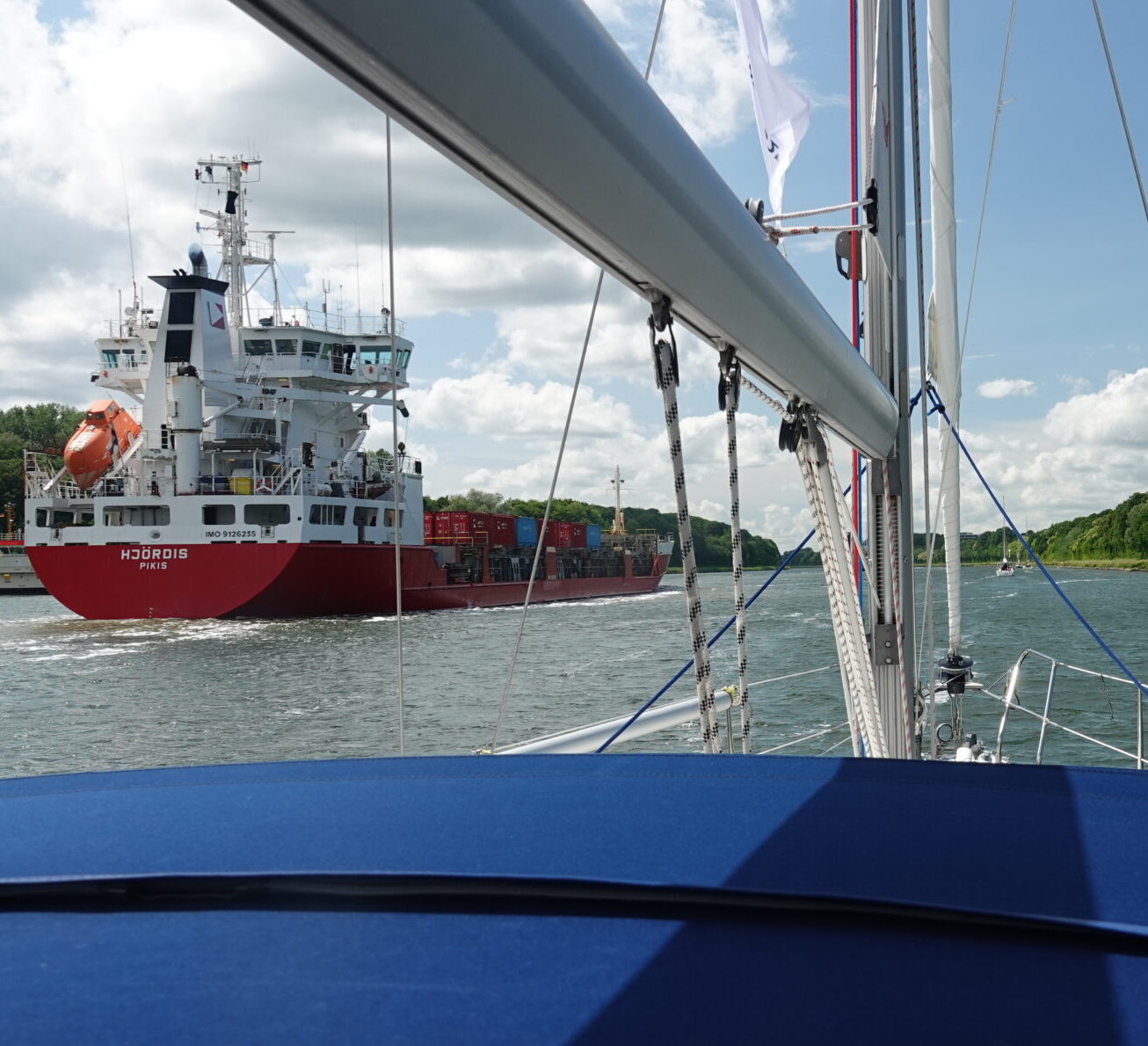 Eine Segelyacht fährt durch den Nord-Ostsee-Kanal hinter einem roten Containerschiff.