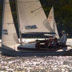 Ein Folkeboot mit weißen Segeln auf glitzerndem Wasser