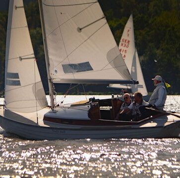 Ein Folkeboot mit weißen Segeln auf glitzerndem Wasser